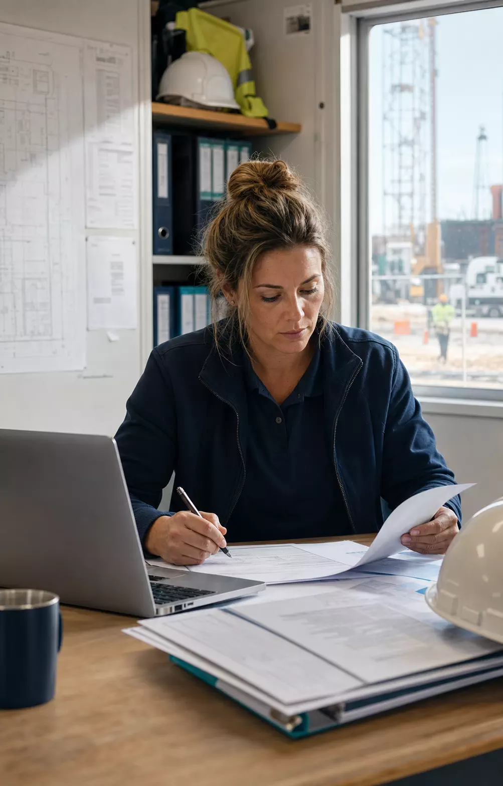 Construction office manager reviewing source documents beside a laptop